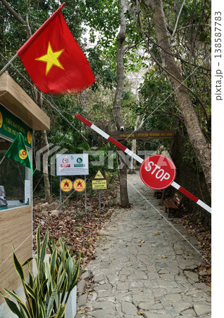 A red and yellow Vietnamese flag flies proudly at the entrance to a natural park, with a stop barrier and signs indicating rules 138587783