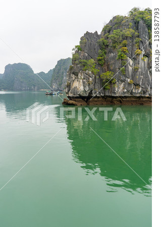 A serene view of limestone karsts rising from emerald waters in Vietnam, with traditional boats navigating the calm sea A serene view of limestone karsts rising from emerald waters in Vietnam, with traditional boats navigating the calm sea 138587793