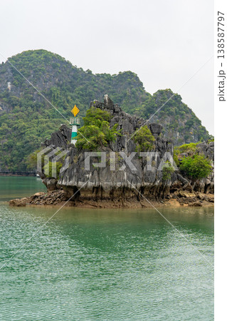 A navigational marker stands atop a rocky island covered in lush green vegetation in Ha Long Bay, Vietnam 138587797