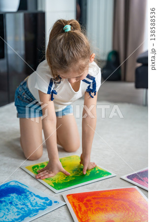 Little girl kneeling on floor pressing colorful sensory gel mats with hands during play activity. Sensory stimulation, autism support and occupational therapy development concept. Little girl kneeling on floor pressing colorful sensory gel mats with hands during play activity. Sensory stimulation, autism support and occupational therapy development concept. 138588536