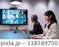 オフィスで大型モニターを使いオンライン会議に参加する男女 オフィスで大型モニターを使いオンライン会議に参加する男女 138589750