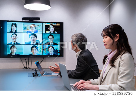 オフィスで大型モニターを使いオンライン会議に参加する男女 138589750