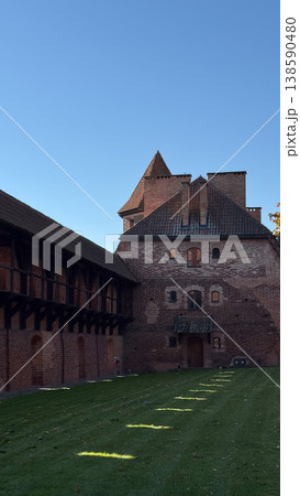 Malbork Castle courtyard with red brick building wooden gallery and grass lawn with sunlight and shadow under clear sky. Architecture, history and travel concept 138590480