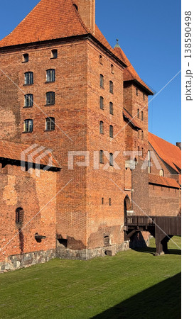 Malbork Castle in Poland with red brick tower wall and wooden bridge over grass courtyard under clear blue sky. Architecture, history and travel concept 138590498