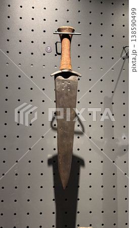 Medieval dagger with wide blade and simple handle displayed on museum wall inside Malbork Castle in Poland. Weapon, history and museum concept Medieval dagger with wide blade and simple handle displayed on museum wall inside Malbork Castle in Poland. Weapon, history and museum concept 138590499