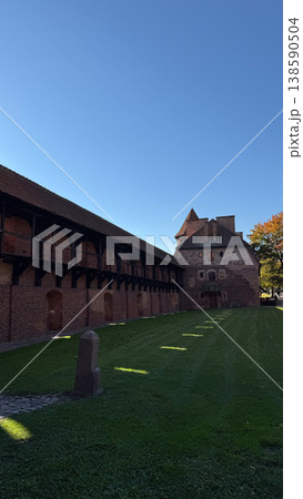 Inner courtyard of Malbork Castle in Poland with red brick buildings wooden gallery and green lawn under clear blue sky. Architecture, history and travel concept 138590504