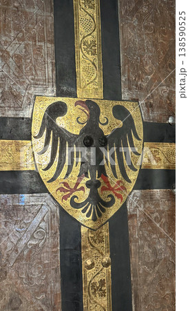 Medieval painted shield with black eagle and decorative cross pattern inside Malbork Castle in Poland. Architecture, history and heraldry concept Medieval painted shield with black eagle and decorative cross pattern inside Malbork Castle in Poland. Architecture, history and heraldry concept 138590525