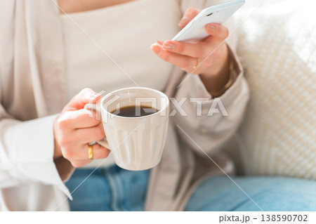 リビングのソファに座りスマホを見る女性の手元 138590702