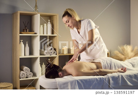 Female therapist massaging clients back in serene wellness spa with candles 138591197