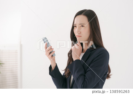 困った表情でスマホを持つスーツの女性 138591263