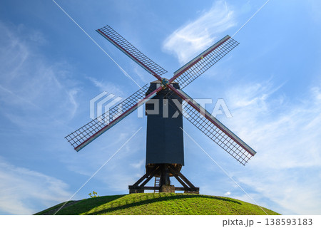 Traditional windmill on grassy hill under blue sky 138593183
