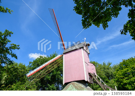 Pink historic windmill under blue sky surrounded by trees Pink historic windmill under blue sky surrounded by trees 138593184