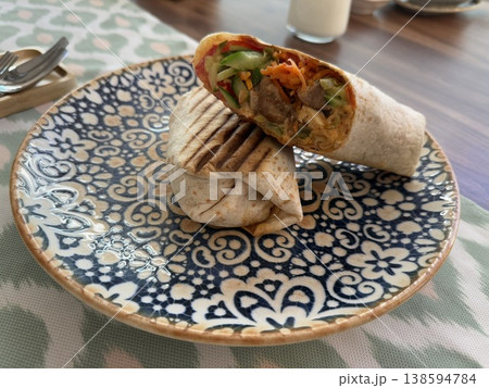 Grilled wrap with vegetables and meat on decorative plate, placed on a wooden table. Grilled wrap with vegetables and meat on decorative plate, placed on a wooden table. 138594784