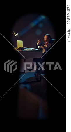 Businesswoman drinking coffee at desk with laptop in dark room seen through keyhole 138594874