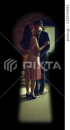 Couple embracing in intimate moment in bedroom seen through keyhole. 138594881