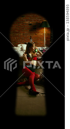 Woman in red lingerie talking on retro phone sitting on floor near bed seen through keyhole Woman in red lingerie talking on retro phone sitting on floor near bed seen through keyhole 138594893