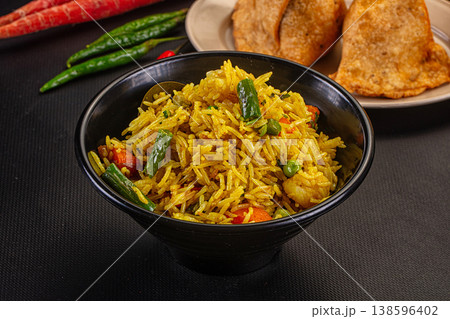 Vibrant Indian vegetable pilaf with fried samosas and raw vegetables on a dark tabletop 138596402