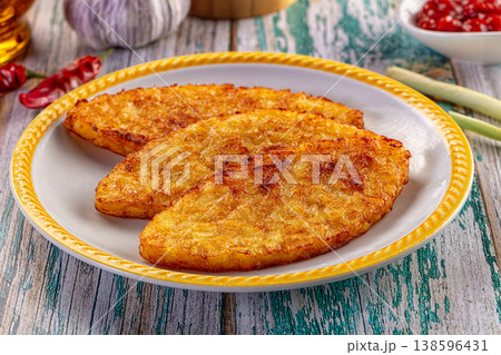 Golden potato pancakes on a plate with fresh ingredients on a rustic wooden table. 138596431