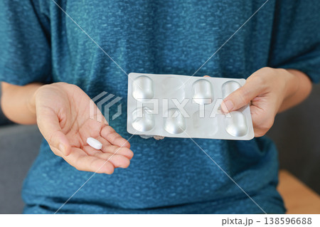 Close up of woman hands holding a white pill and an aluminum blister pack. Taking medicine, healthcare, pharmacy, painkiller, antibiotic or vitamin concept. Medical treatment for illness and health. Close up of woman hands holding a white pill and an aluminum blister pack. Taking medicine, healthcare, pharmacy, painkiller, antibiotic or vitamin concept. Medical treatment for illness and health. 138596688