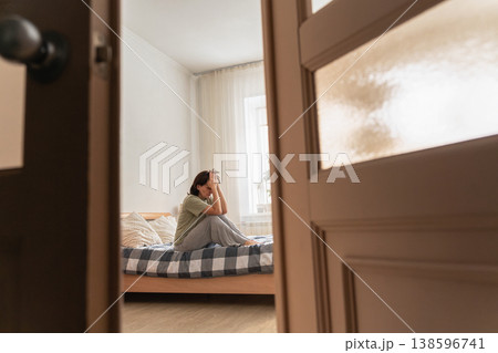 An adult woman sitting on bed with head in hands, struggling with sadness, grief, and mental health issues. Feeling lonely and isolated An adult woman sitting on bed with head in hands, struggling with sadness, grief, and mental health issues. Feeling lonely and isolated 138596741
