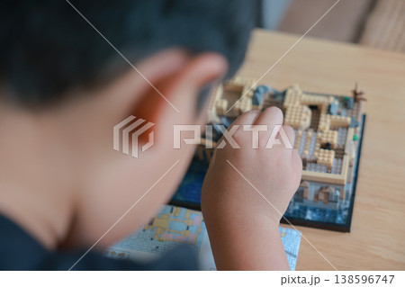 Close up of child hand assembling micro building blocks with instruction manual on wooden table. Little boy playing educational toy. Kids development, creativity, concentration and learning concept. Close up of child hand assembling micro building blocks with instruction manual on wooden table. Little boy playing educational toy. Kids development, creativity, concentration and learning concept. 138596747
