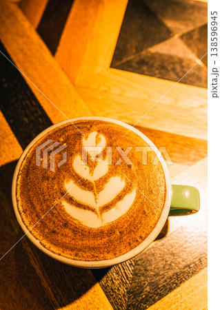 Latte art, a coffee drink with frothed milk creating a leaf pattern, resting on a geometric wooden table. A mug of hot fresh coffee creating a cozy atmosphere Latte art, a coffee drink with frothed milk creating a leaf pattern, resting on a geometric wooden table. A mug of hot fresh coffee creating a cozy atmosphere 138596945