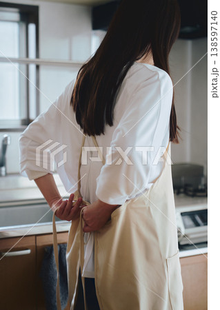 キッチンでエプロンをつける女性 家事や料理準備の生活シーン 138597140