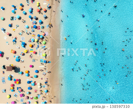 Aerial view of colorful umbrellas on sandy beach, swimming people 138597310