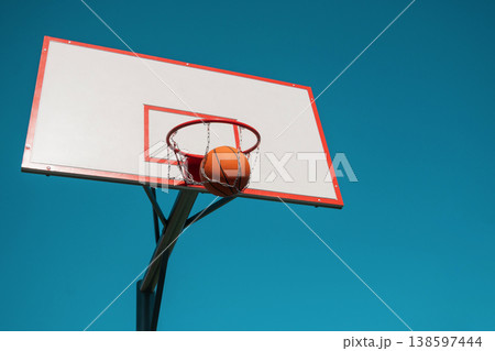 Basketball ball inside hoop with chain net minimal sky background Basketball ball inside hoop with chain net minimal sky background 138597444