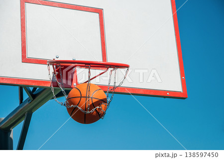 Basketball ball scoring through hoop with chain net against blue sky 138597450
