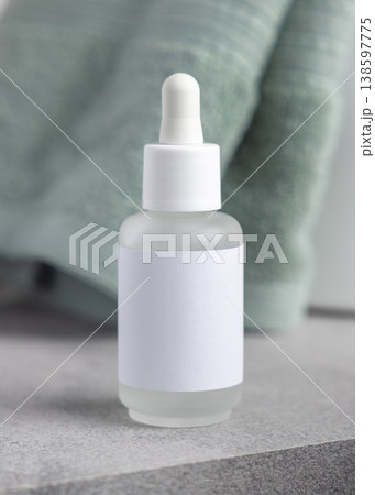Glass dropper bottle with blank label mockup near light green bath towel, unbranded packaging Glass dropper bottle with blank label mockup near light green bath towel, unbranded packaging 138597775