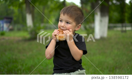 Three year old boy eats cheeseburger outdoors and looks at camera portrait 4k Three year old boy eats cheeseburger outdoors and looks at camera portrait 4k 138598172