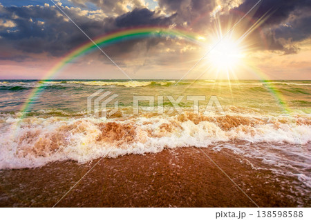 stormy weather on the sandy beach at sunset. dramatic sky over the sea in evening light. moody summer landscape. green waves crashing the shore. majestic cloudscape and rainbow above the horizon 138598588