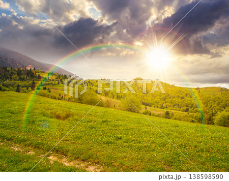 remote countryside in mountain landscape at sunset. hazy weather during spring in evening light. dirt road through lush green pasture on a hill. alpine vista with deciduous trees under rainbow remote countryside in mountain landscape at sunset. hazy weather during spring in evening light. dirt road through lush green pasture on a hill. alpine vista with deciduous trees under rainbow 138598590
