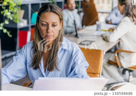 Experienced Manager Carefully Examining Spreadsheets While Surrounded By Colleagues In Professional Setting Experienced Manager Carefully Examining Spreadsheets While Surrounded By Colleagues In Professional Setting 138598686