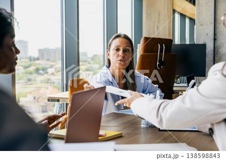 Woman Reviewing Documents. Woman Concentrates On Report While Coordinator Offers Approval Documents Nearby Woman Reviewing Documents. Woman Concentrates On Report While Coordinator Offers Approval Documents Nearby 138598843