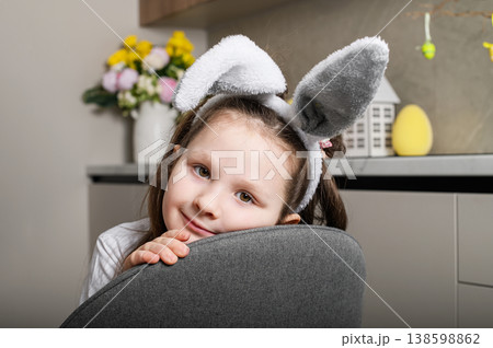 Cute girl in bunny ears leaning on chair in kitchen interior Cute girl in bunny ears leaning on chair in kitchen interior 138598862