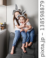 Two children in bunny ears sitting together on sofa in living room. Easter holiday, friendship, sibling relationship and family lifestyle concept. 138598879