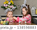 Two girls painting Easter eggs at table in kitchen 138598883