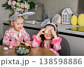 Two girls painting Easter eggs at table in kitchen 138598886