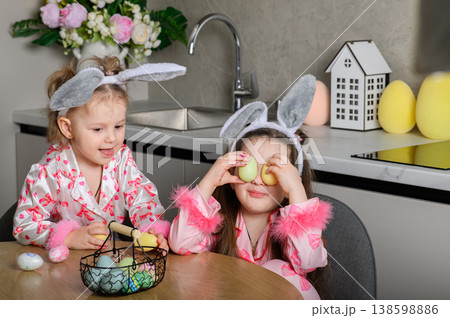 Two girls painting Easter eggs at table in kitchen 138598886