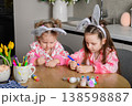 Two girls painting Easter eggs at table in kitchen 138598887