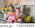 Two little girls in bunny ears holding tulips in kitchen 138598888