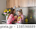 Two little girls in bunny ears holding Easter basket with eggs in kitchen 138598889
