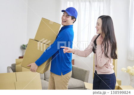 段ボールを持つ引っ越し業者と笑顔で指示する女性 138599824
