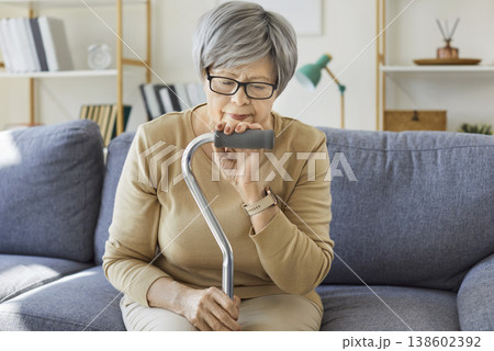 Senior woman with cane sitting alone on sofa at home, sad person thinking 138602392