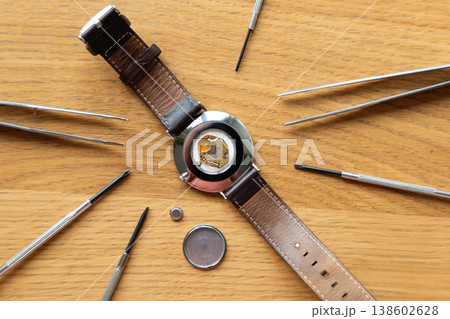 Watch with leather strap and opened back placed on wooden surface surrounded by watch repair tools including tweezers Watch with leather strap and opened back placed on wooden surface surrounded by watch repair tools including tweezers 138602628