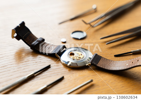 Watch components displayed on a wooden surface, featuring a dismantled wristwatch with leather strap and tools arranged around it Watch components displayed on a wooden surface, featuring a dismantled wristwatch with leather strap and tools arranged around it 138602634