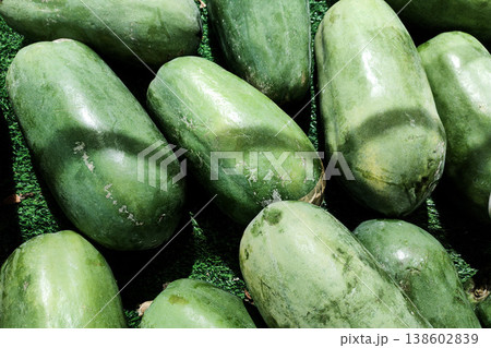 Fresh Green Papayas Laying on a Green Surface at a Market, Displaying Natural Texture and Color, Perfect for Tropical Fruit Imagery Fresh Green Papayas Laying on a Green Surface at a Market, Displaying Natural Texture and Color, Perfect for Tropical Fruit Imagery 138602839