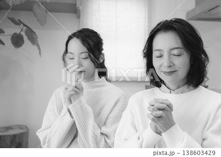 自宅で故人に祈りを捧げる母と娘（モノクロ） 138603429